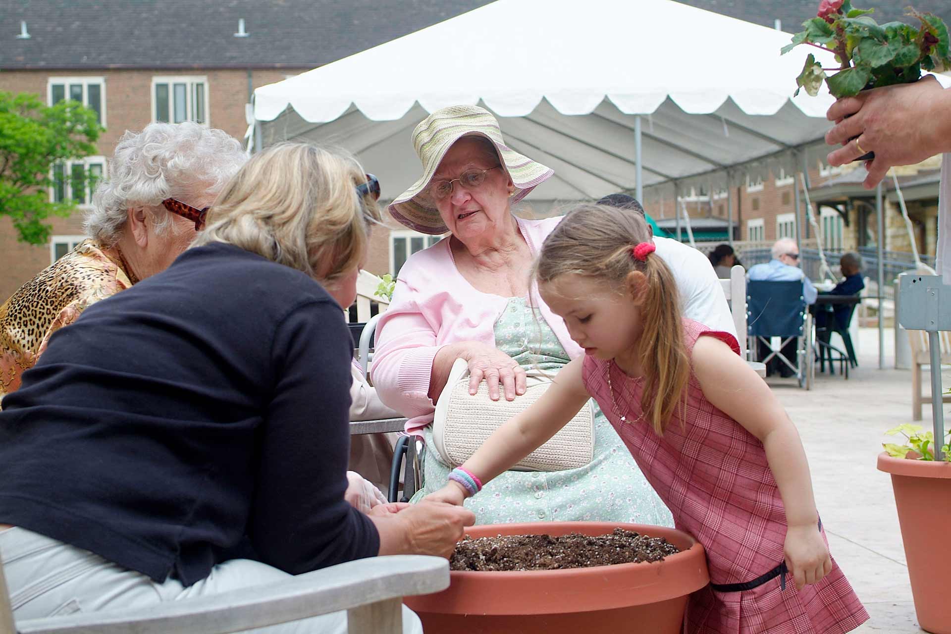 A photo of residents and a child planting flowers in pots outside The McGregor.