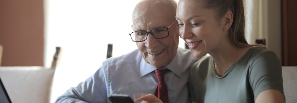 An older man looking at a cell phone with a younger woman