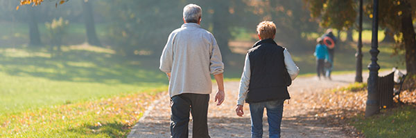 An elderly man and woman walking on a road outside 