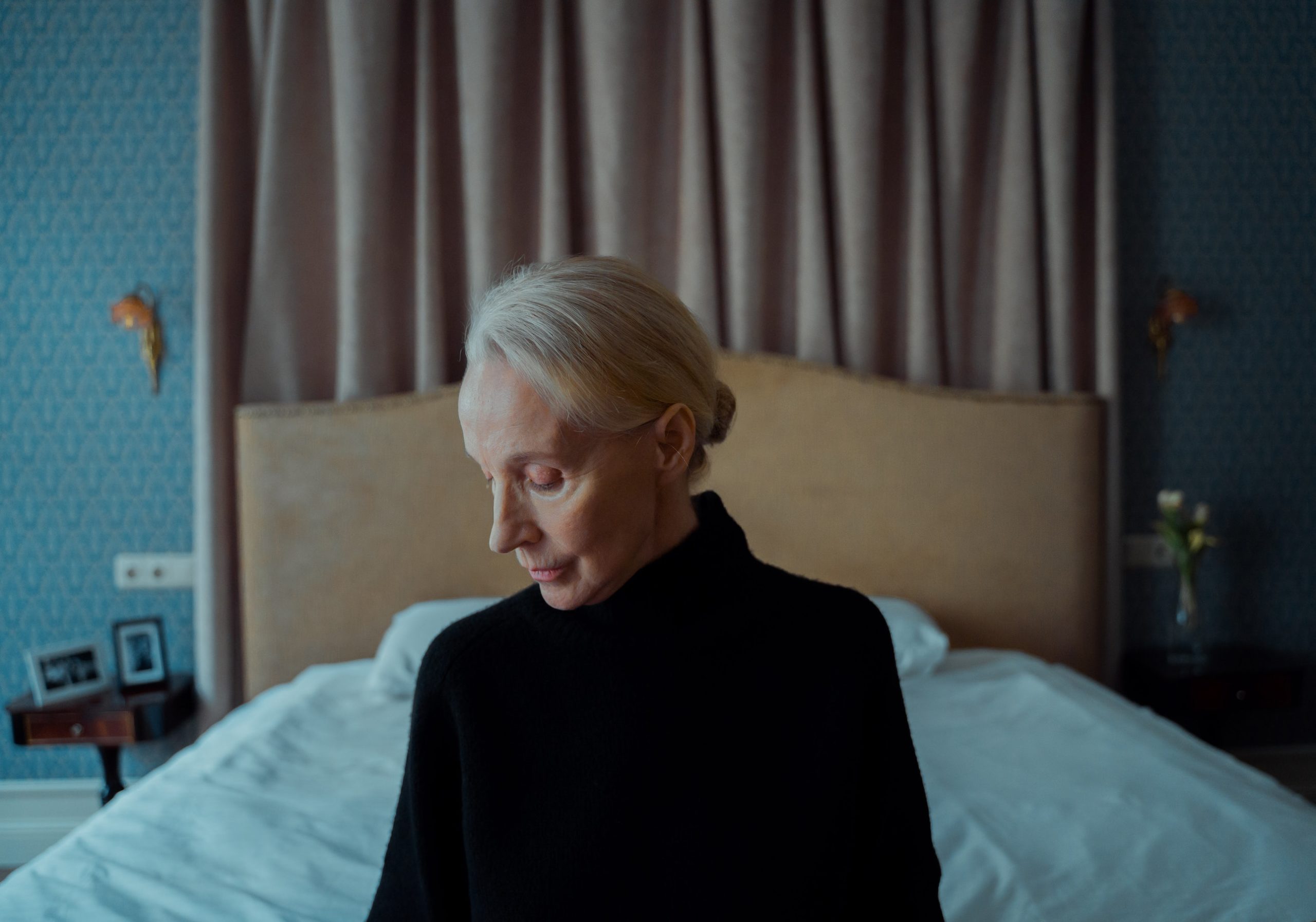 older woman sitting on a bed looking at the ground