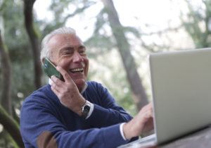 man smiling holding cell phone looking at laptop