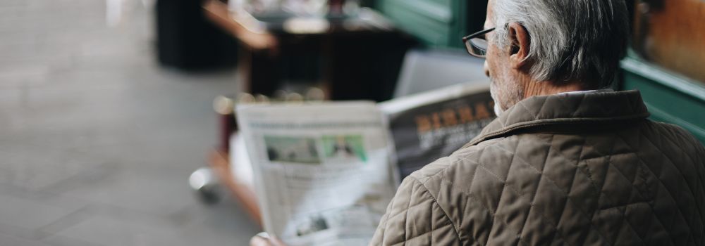elderly man reading newspaper outside