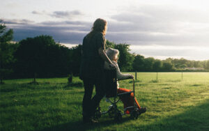 A woman pushing an elderly woman in a wheelchair through an open field