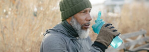 An elderly man sitting on a park bench drinking water from a sports water bottle