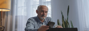 An elderly man sitting at a table holding his phone and credit card