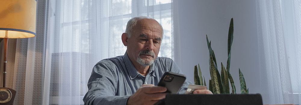 An elderly man sitting at a table holding his phone and credit card