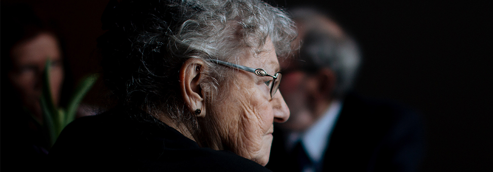 A close up of an elderly woman with glasses sitting in a dark room