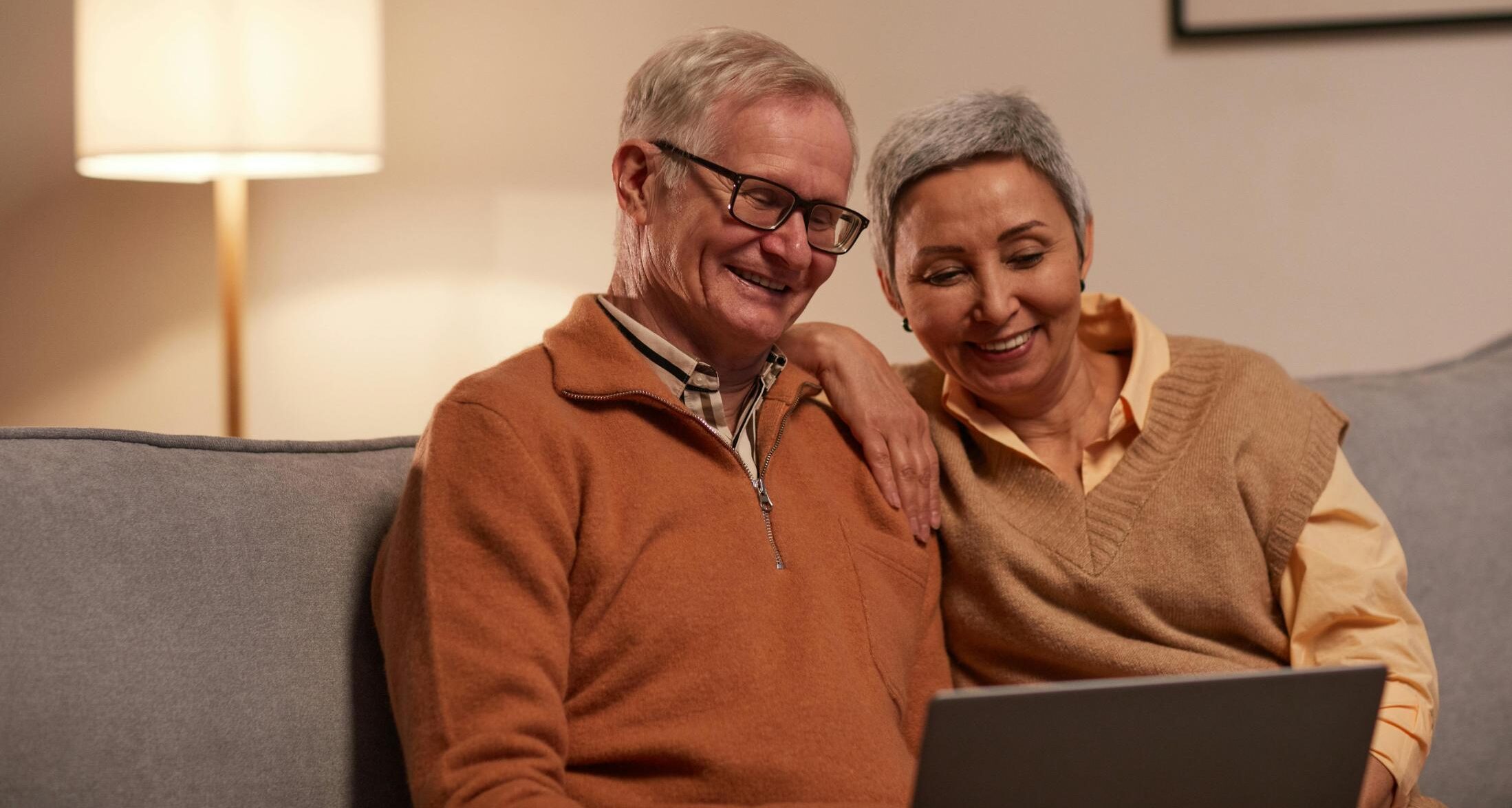 two older couple cuddled on a couch smiling at a laptop