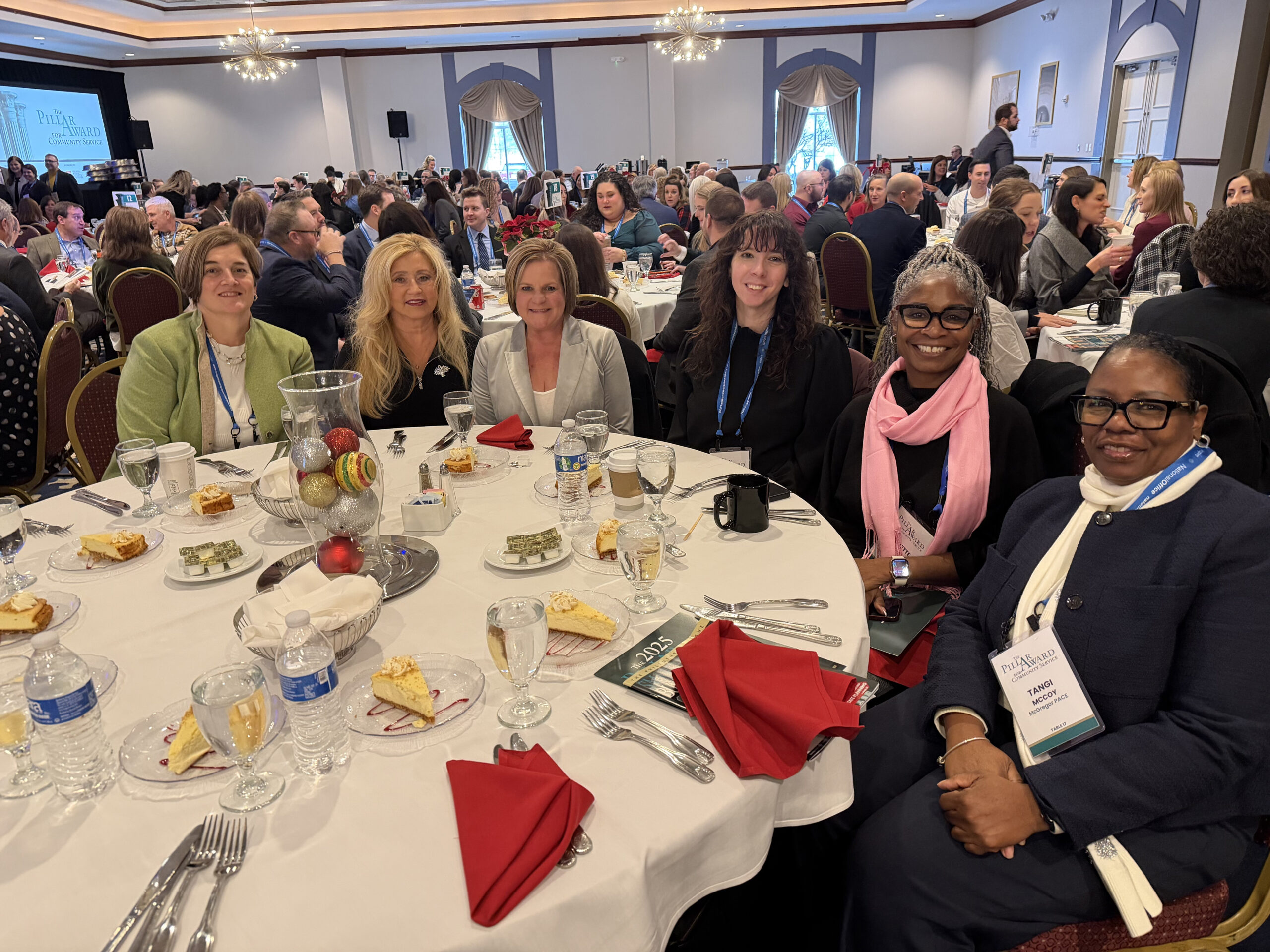 A group of diverse adults gathered at a round table and smiling at the camera, appearing to be eating dessert.