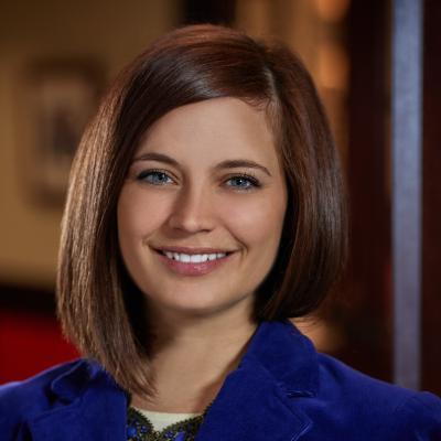 A person with short brown hair, wearing a blue jacket, smiling.