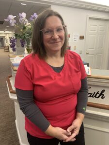 A person in a red scrub top stands in an indoor setting, possibly a healthcare facility.