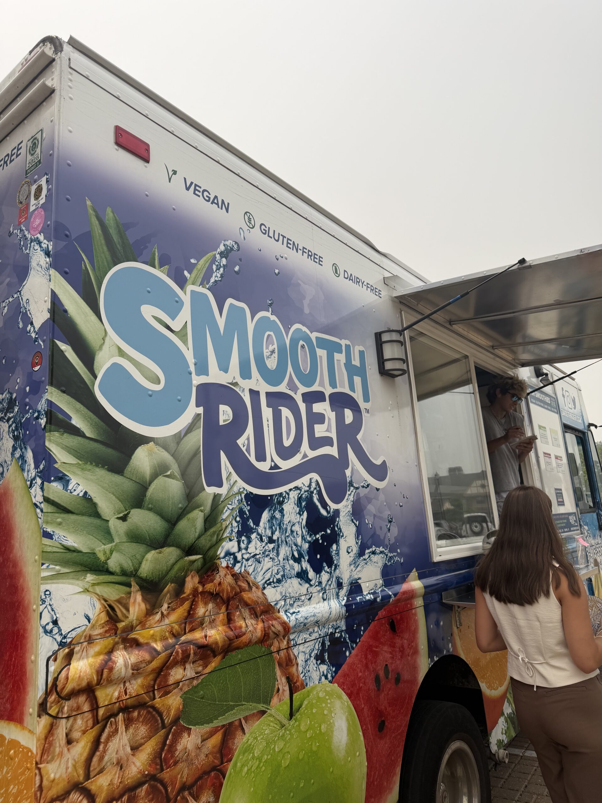 A colorful smoothie truck named "Smooth Rider," featuring fruits like pineapple and apple, offering vegan and gluten-free options.